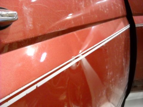 1993 Ford C-150 (Centurion Conversions) - A dent is visible on the side of a red vehicle door, near the chrome door handle and white pinstripe.