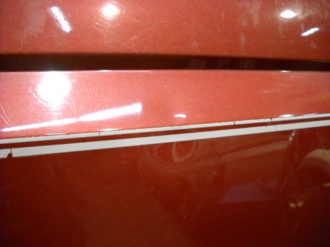 1993 Ford C-150 (Centurion Conversions) - Close-up of a dent on a red vehicle's side panel with white pinstripes.