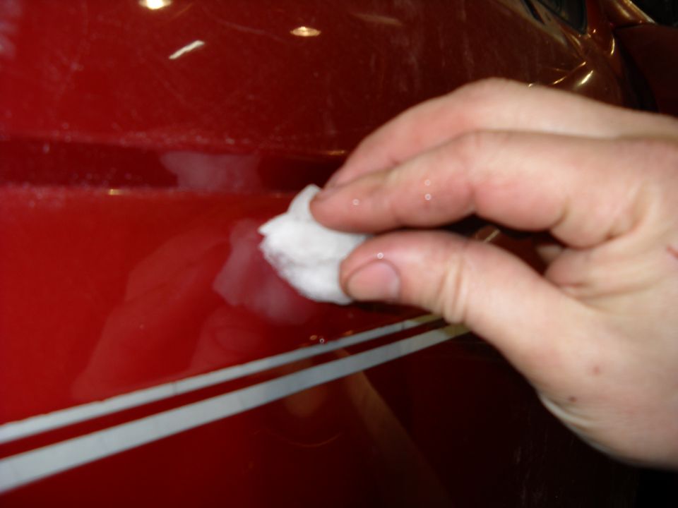 Hand with cotton ball cleaning a red vehicle side with white stripe