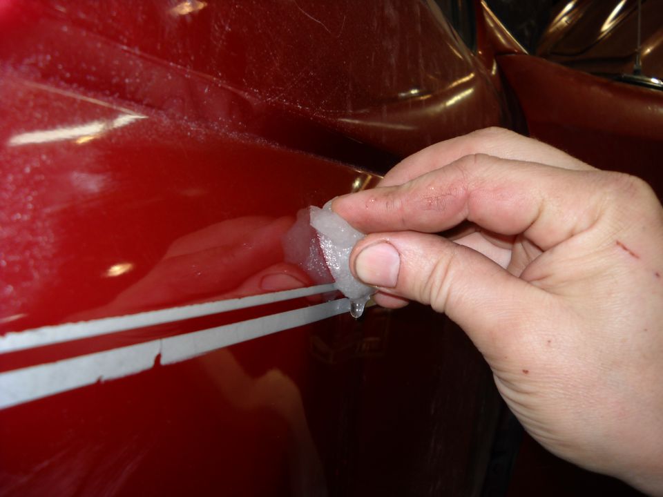 Hand removing white stripe decal from red vehicle side