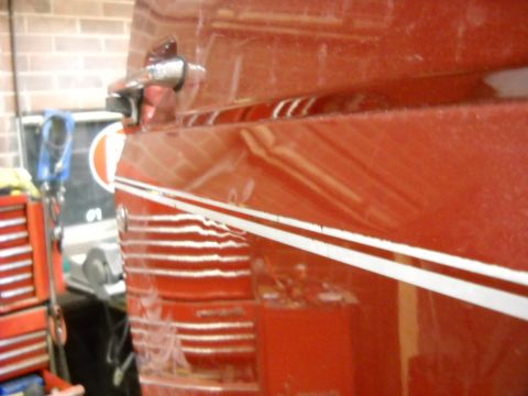 1993 Ford C-150 (Centurion Conversions) - Close-up of a red truck door with visible damage and white pinstripes, in a workshop setting.