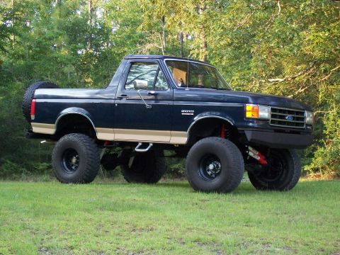 1990 Ford Bronco - A lifted 1990 Ford Bronco sits on a grassy field with trees in the background.