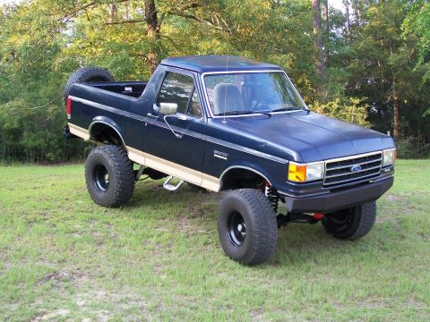 1990 Ford Bronco - This lifted 1990 Ford Bronco is parked on a grassy field with trees in the background.