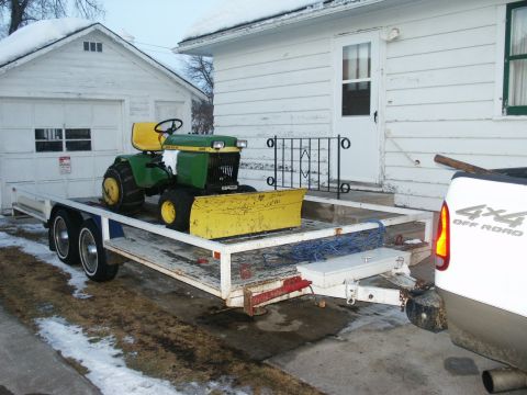 1966 Ford Bronco - A green and yellow tractor with a snow plow is loaded onto a trailer in front of a white house and garage.