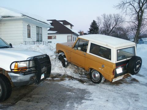 1966 Ford Bronco - A yellow 1966 Ford Bronco is stuck in the snow next to a white truck.