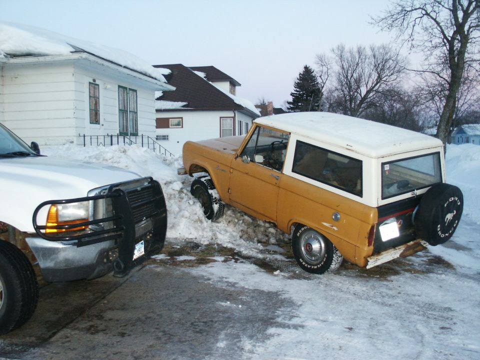 Yellow 1966 Ford Bronco with a white hardtop stuck in snow, viewed from the front 3/4 angle