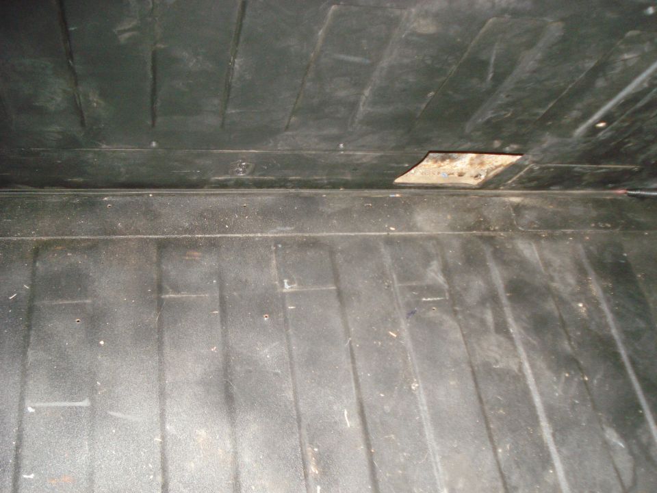 Dark, textured interior of a vehicle cargo area with visible wear and a small damaged section on the ceiling