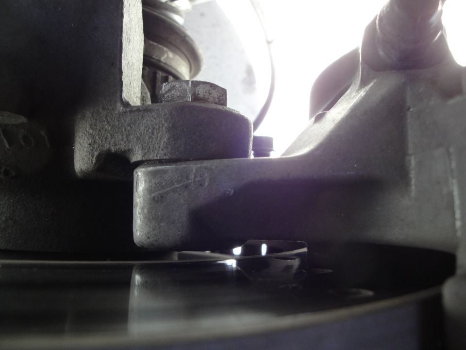 Close-up of a vehicle's brake caliper and rotor assembly. A bolt secures a bracket to the caliper