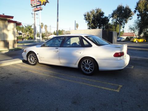 1993 Ford Taurus - White sedan parked in a lot with a yellow car visible in the distance.