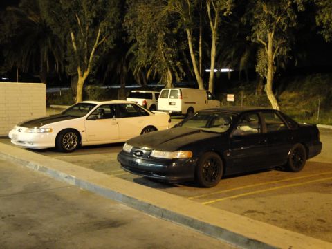 1993 Ford Taurus - A dark sedan is parked in a lot, with a white sedan and a van behind it.