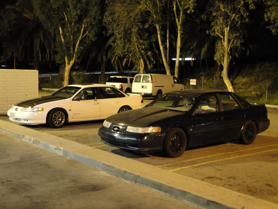 Dark sedan with black rims parked in a lot at night