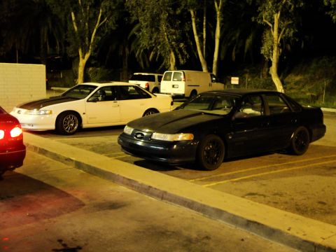1993 Ford Taurus - A black sedan is parked in a lot at night, showing its front three-quarter view. The vehicle appears to be a 1995 model.