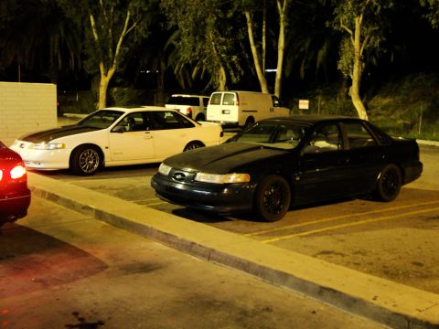 1993 Ford Taurus - Multiple vehicles parked in a lot at night, including a black sedan and a white sedan.
