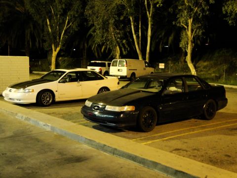 1993 Ford Taurus - A black sedan is parked in a lot at night, with another white car visible behind it.