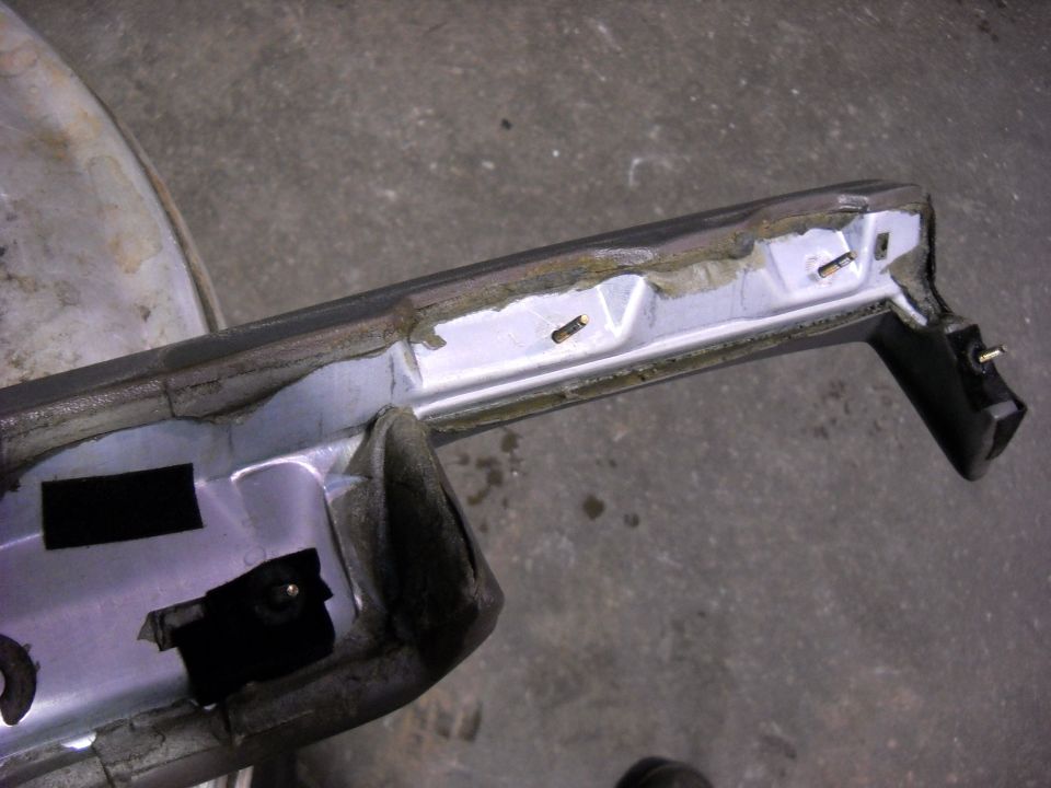 Underside of removed white body panel on garage floor showing seam sealer, welds and mounting clips