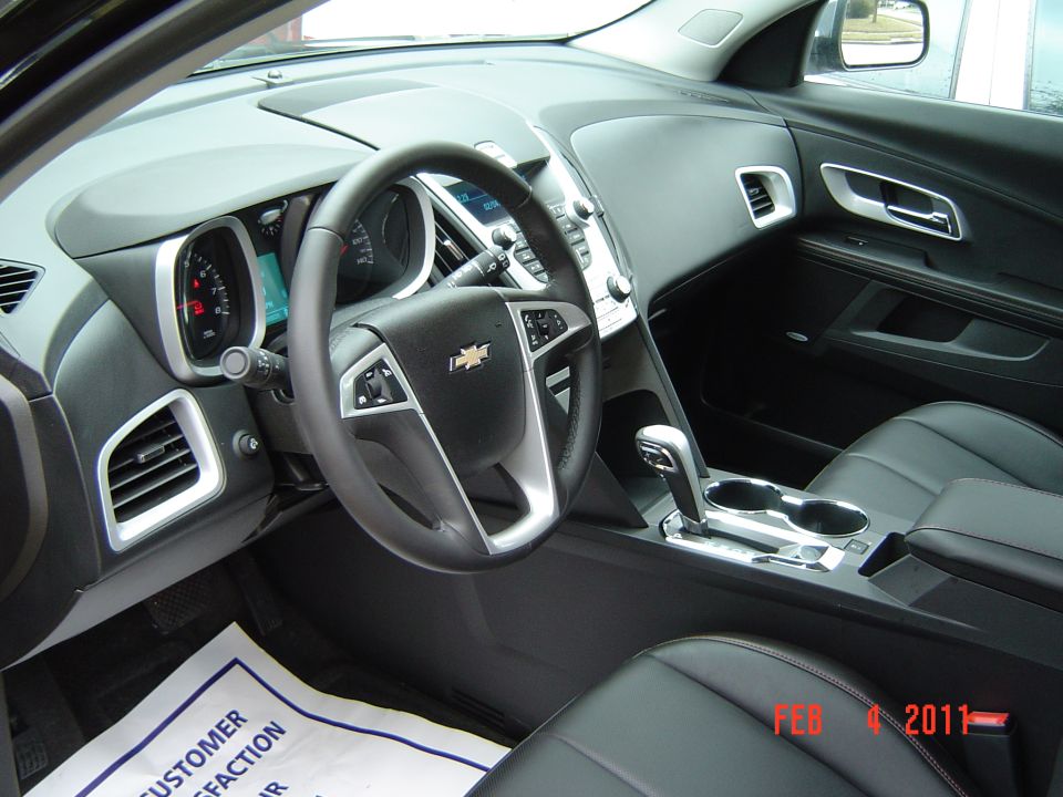 Black Chevrolet Equinox interior with leather steering wheel, silver trim, and dealer paper floor mat