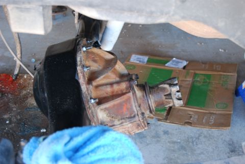 1982 Ford Bronco - A close-up view of a rear axle differential, showing its rusty and worn components, with a blue cloth partially obscuring the foreground.
