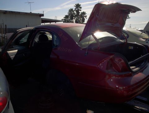 2003 Ford Taurus - A red sedan sits in a junkyard with its doors and trunk open, showing some handwritten markings on its body.