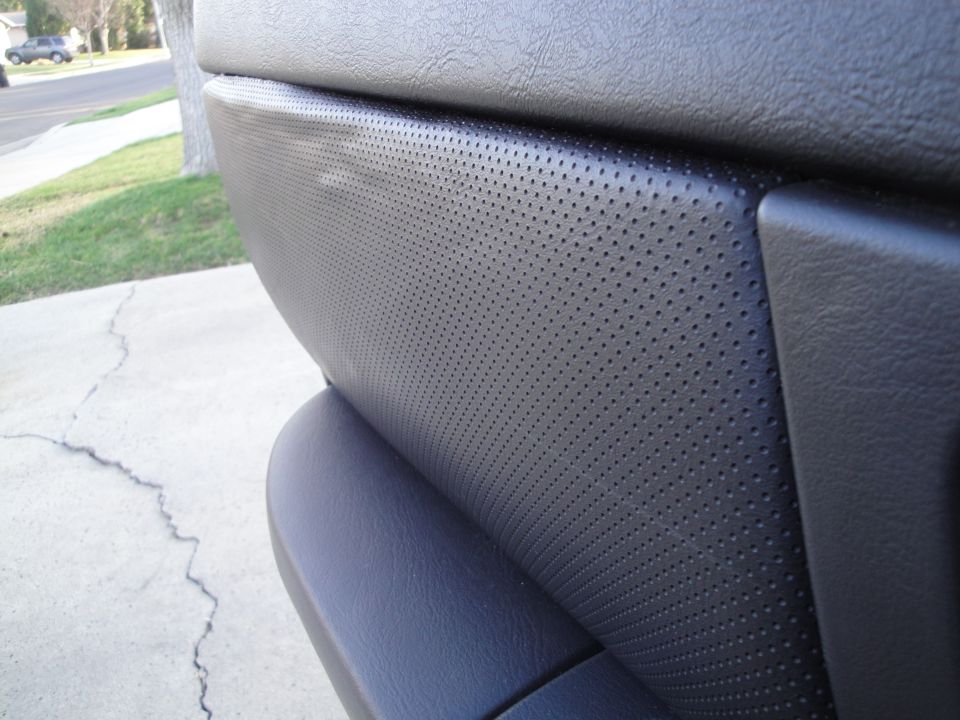 Close-up of gray perforated leather door panel insert with grained plastic trim, door open in driveway
