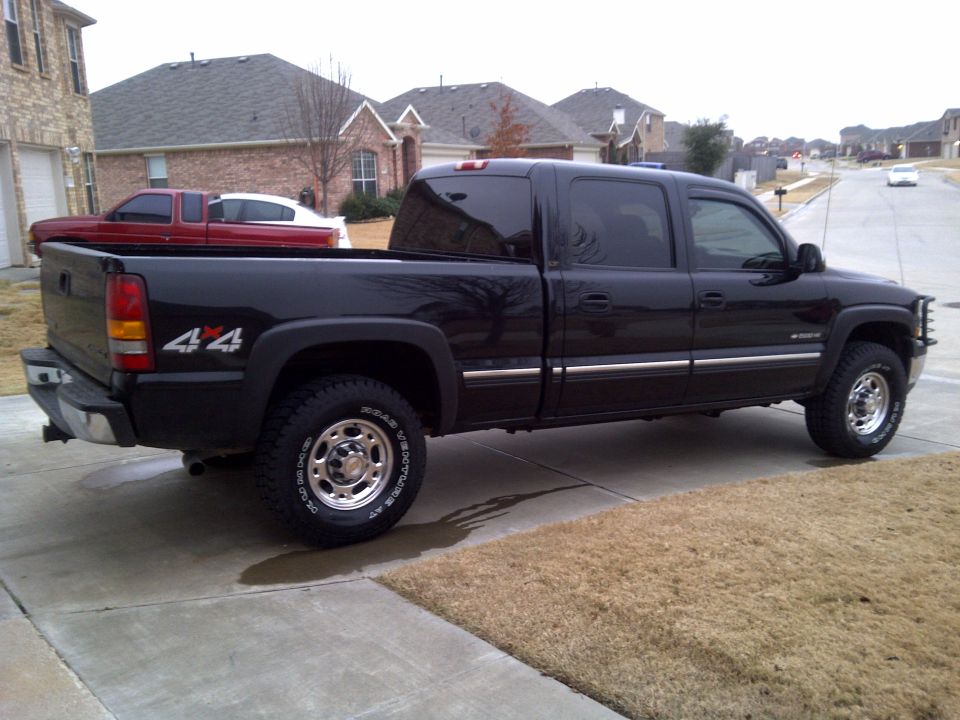 Black 2002 Chevrolet Silverado 1500 crew cab pickup truck parked on driveway, red pickup truck in background