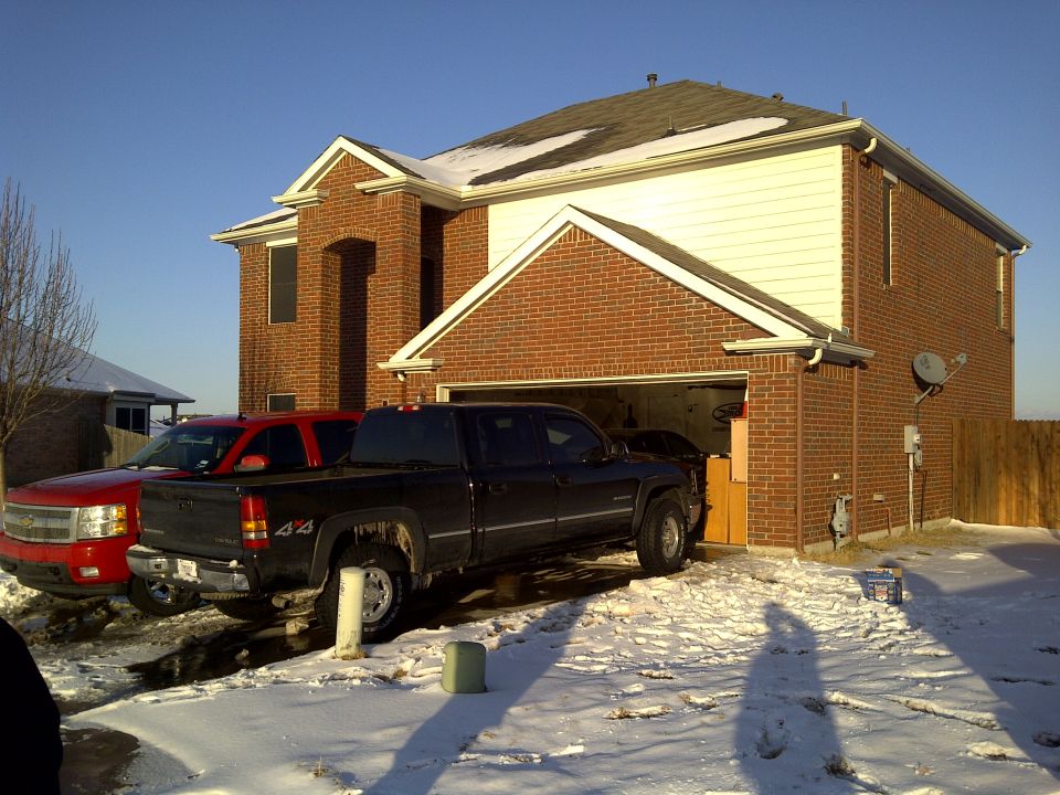 Black Chevrolet Silverado pickup truck with 4x4 badging and a red Chevrolet Avalanche pickup truck parked in a snowy driveway