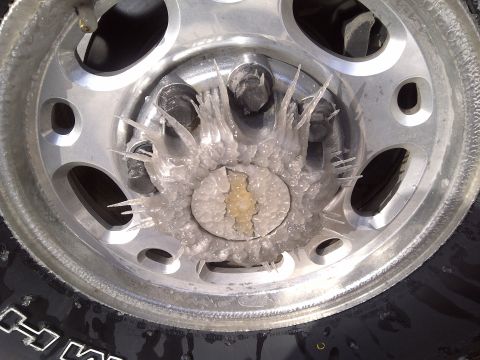 2002 Chevrolet Silverado 1500 - Ice formations have created icicles around the Chevrolet emblem on the wheel hub of a vehicle.