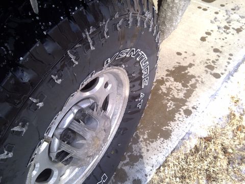 2002 Chevrolet Silverado 1500 - A tire covered in ice, suggesting cold weather conditions. The 'VENTURE AT' branding is visible on the tire sidewall.