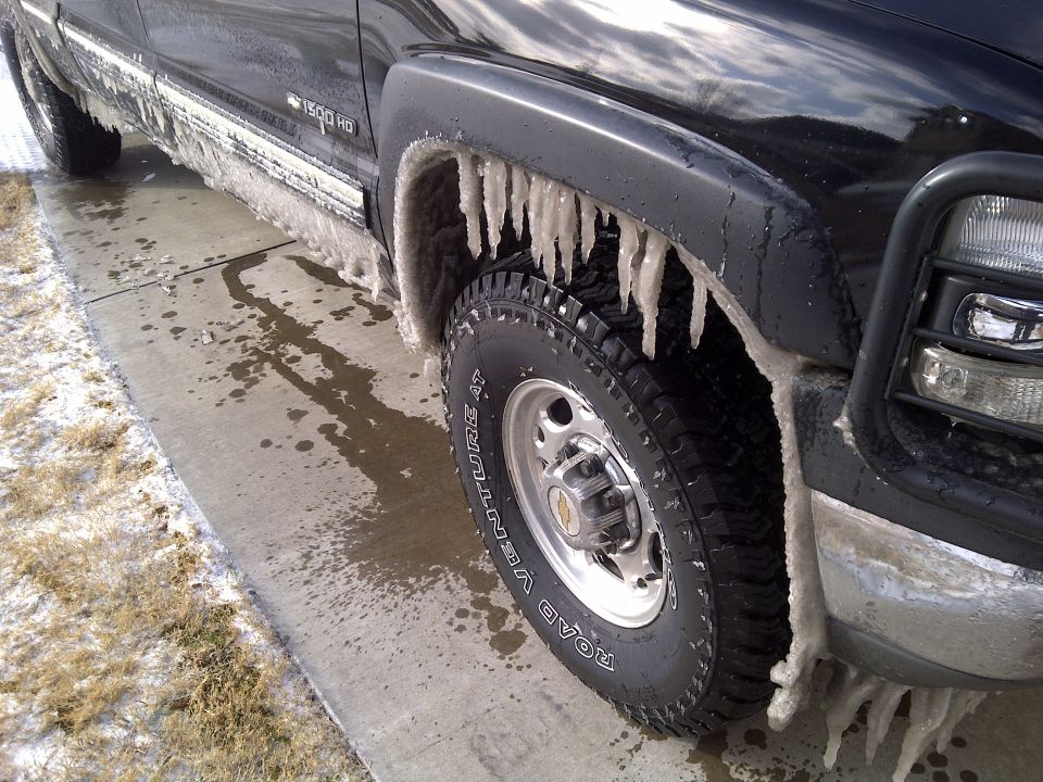 Side view of a black pickup truck covered in ice, with icicles hanging from the fender