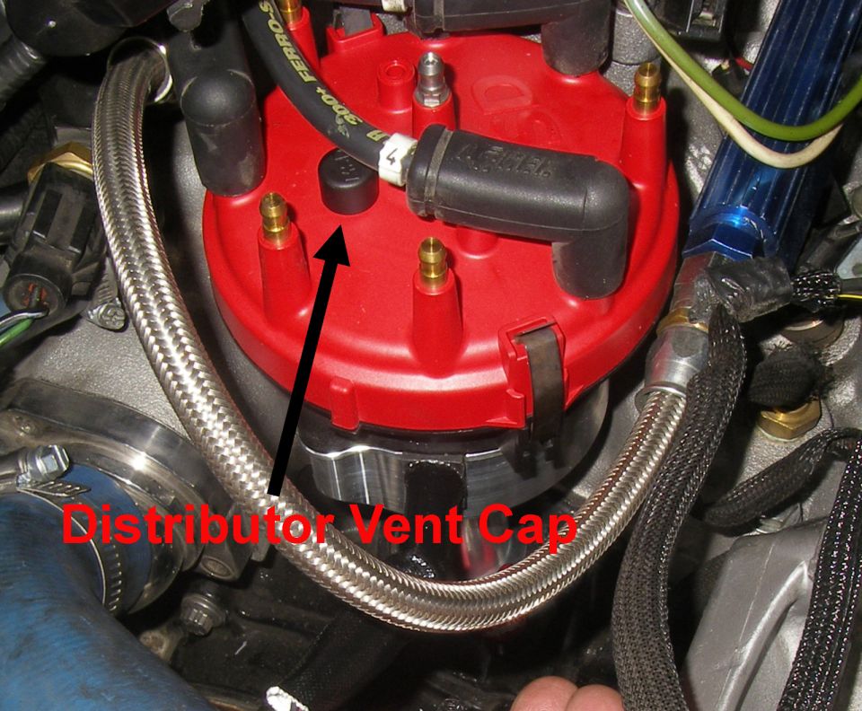 Red distributor cap with arrow labeling the vent cap in an engine bay