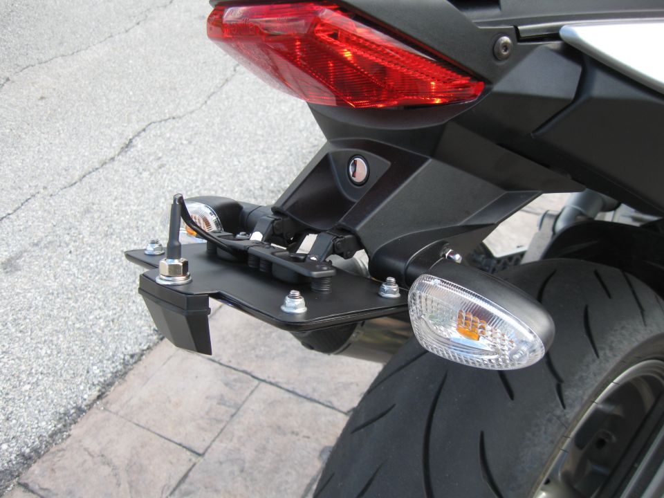Rear tail of black motorcycle with red taillight, clear turn signals, and fender eliminator bracket, plate removed