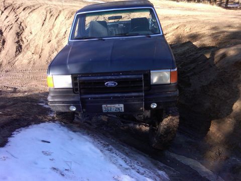 1988 Ford Bronco - This Ford Bronco is driving on a dirt path with some snow on the ground.