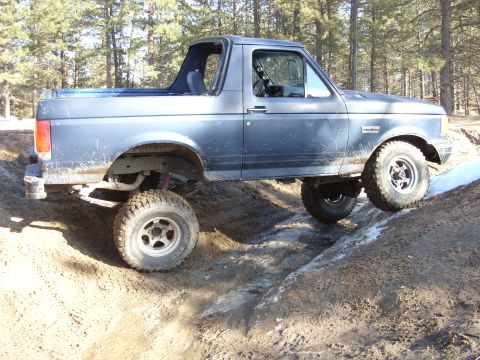 1988 Ford Bronco - This blue Ford Bronco is navigating a challenging off-road course with muddy terrain and some icy patches.