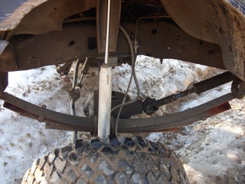 1988 Ford Bronco - The underside of a vehicle shows its suspension components and a large tire in the snow.