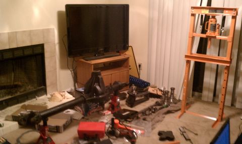 1990 Ford Bronco - Various automotive parts are scattered around a room, with a hydraulic press standing tall.