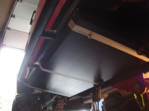 1989 Ford Bronco - A low-angle shot reveals the underside of a vehicle, focusing on its large tires and a black panel affixed to the chassis.