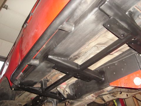 1989 Ford Bronco - Underside view of a red vehicle with extensive black frame reinforcements and visible rust.