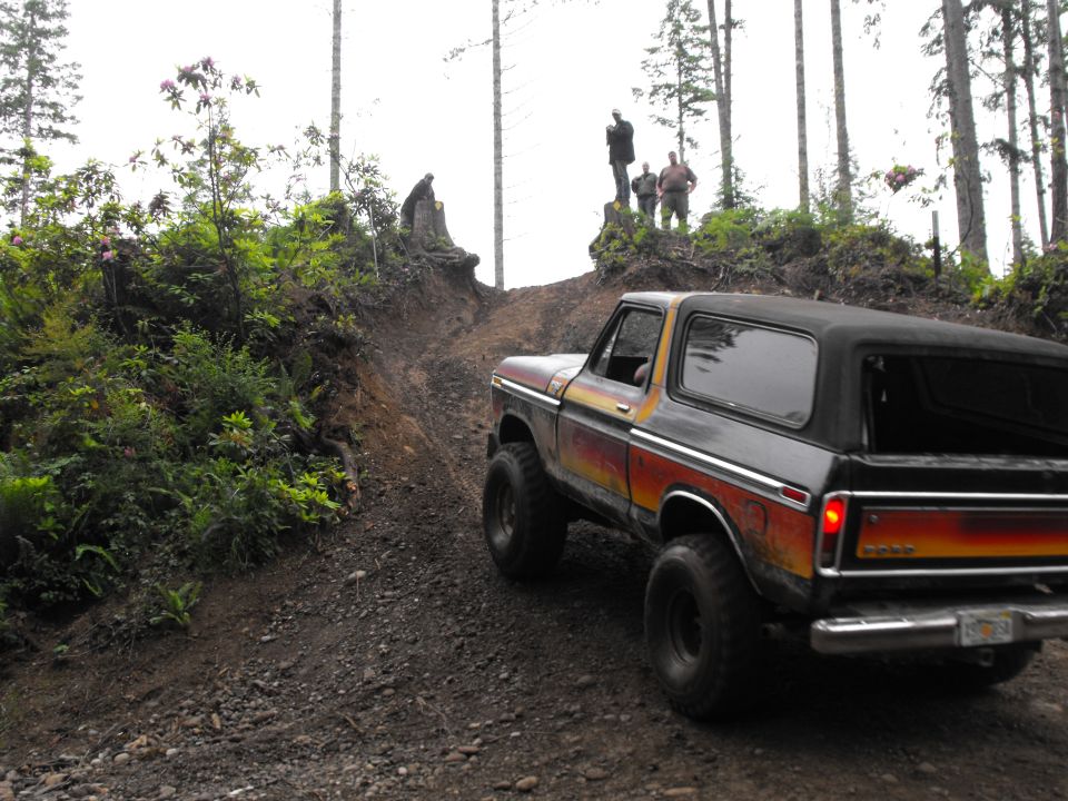 Lifted black Ford Bronco with flame graphics on a rutted dirt trail in the woods