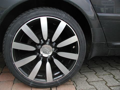2003 Audi A6 - Close-up of a car's wheel and tire, a multi-spoke design and visible tire sidewall text. The 'SUPERMOTORS' watermark is present.