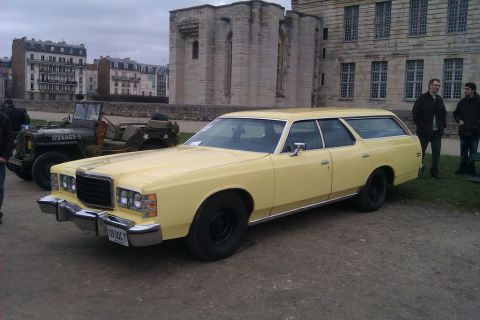 1991 Ford LTD Crown Victoria - A yellow station wagon is parked in front of a large stone building, with a military jeep to its left.