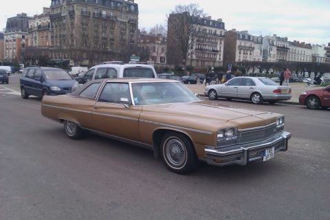 1991 Ford LTD Crown Victoria - A gold 1976 Buick LeSabre coupe is seen in traffic on a city street with other vehicles and buildings in the background.