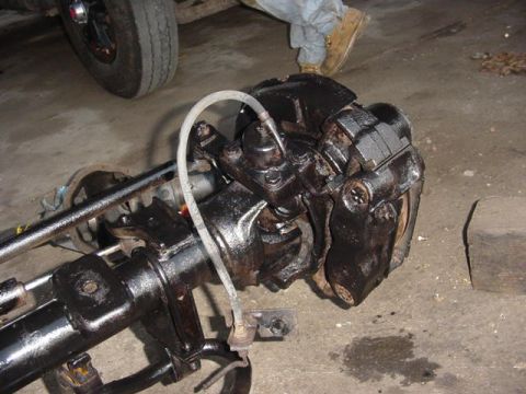 1992 Ford Bronco - Close-up of a freshly painted black solid front axle end on a garage floor, showing the steering knuckle, hub flange with disc brake calipe…