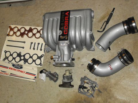 1994 Ford Bronco - Ford 5.0 Cobra intake manifold and associated parts laid out on the floor.
