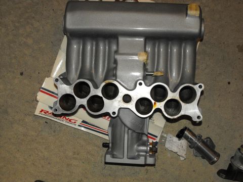 1994 Ford Bronco - A silver intake manifold is shown, with visible ports and resting on a box of racing performance parts.