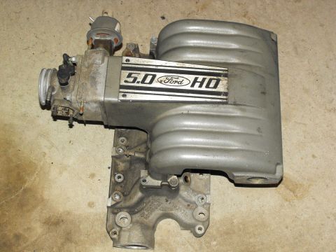 1994 Ford Bronco - A Ford 5.0 HO intake manifold is shown, detached from a vehicle and resting on a concrete surface.