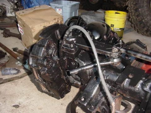 1992 Ford Bronco - A greasy differential axle assembly sits on the floor next to a cardboard box and a yellow bucket.