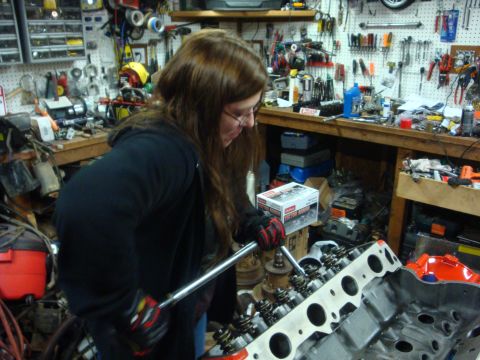 1989 Ford Bronco - A person uses a torque wrench on an engine's valve train in a workshop filled with tools and automotive parts.