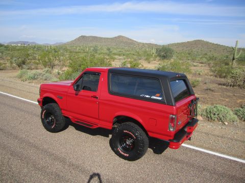 1996 Ford Bronco - A red 1996 Ford Bronco is parked on the side of a desert road under a clear blue sky.