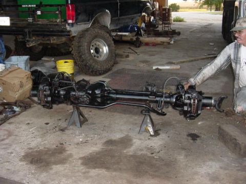 1992 Ford Bronco - A man inspects a front axle assembly that is on jack stands in a garage.