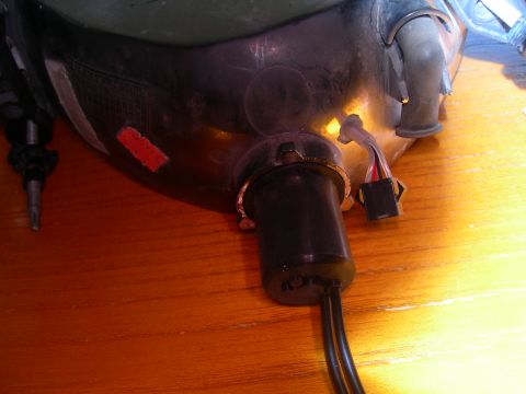1984 Ford Bronco - Close-up view of a vehicle headlight assembly, showing electrical connections and a red adhesive sticker.
