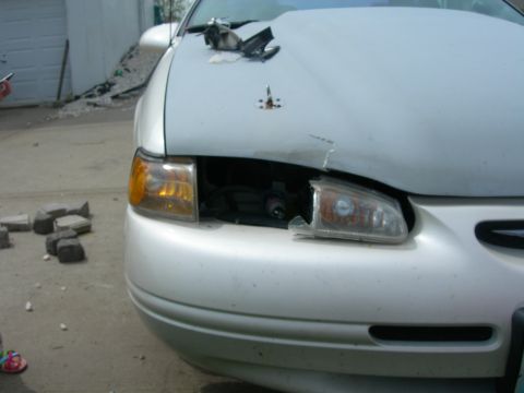 1984 Ford Bronco - Front view of a damaged white car, showing a missing headlight and dented hood.